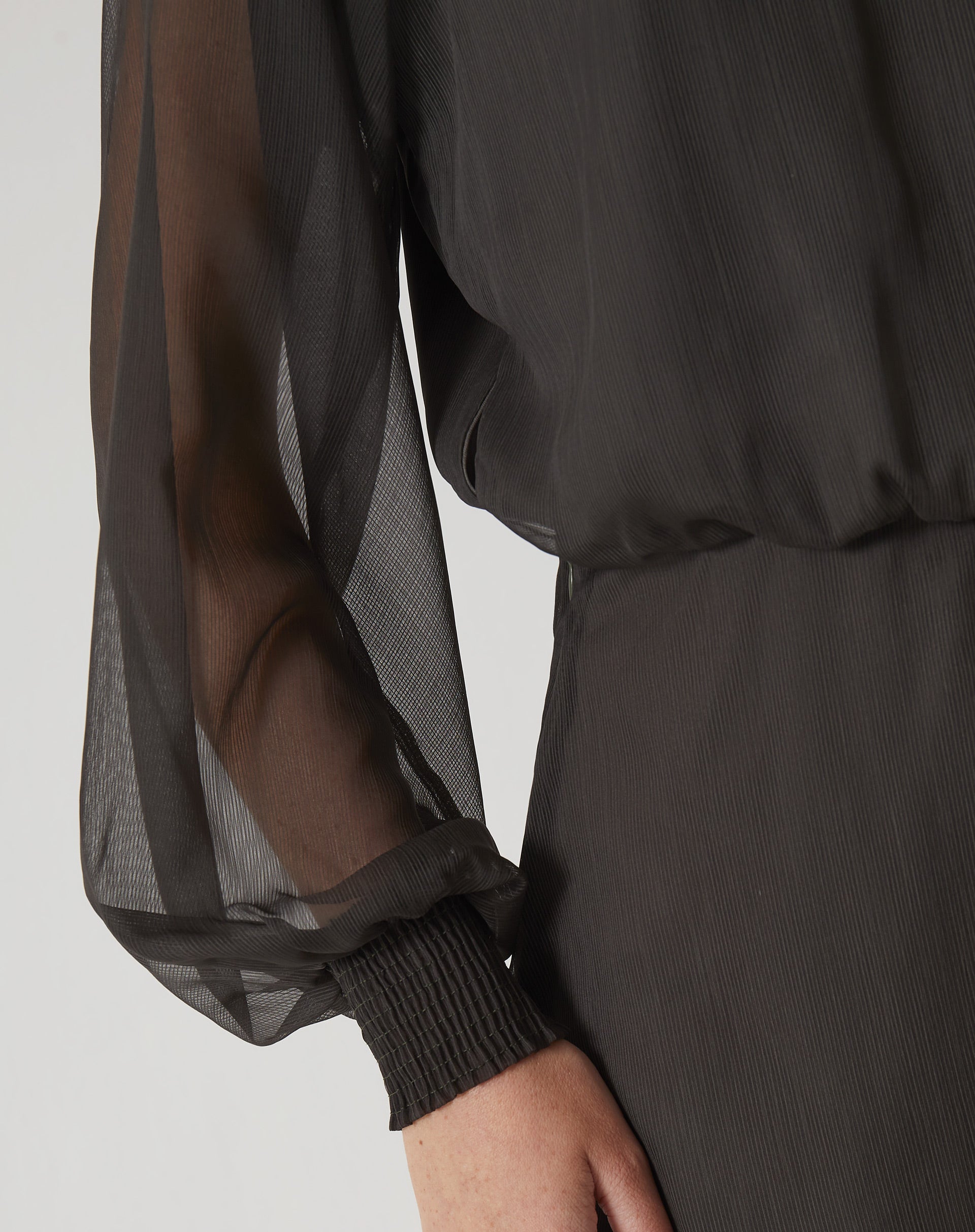 Detalhe da manga longa bufante do vestido curto verde, com punho ajustado.