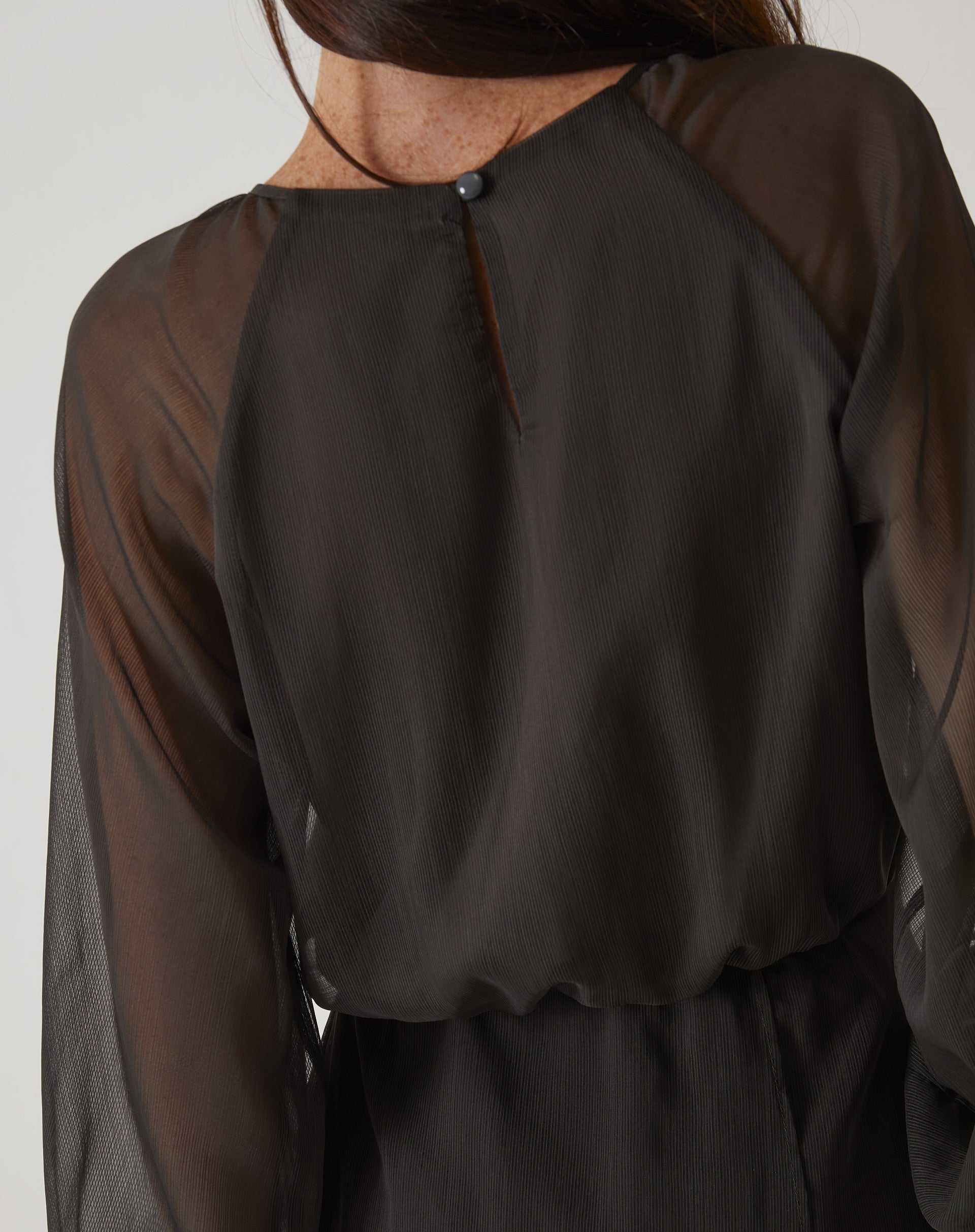 Close-up do fechamento traseiro do vestido curto verde, com botão.