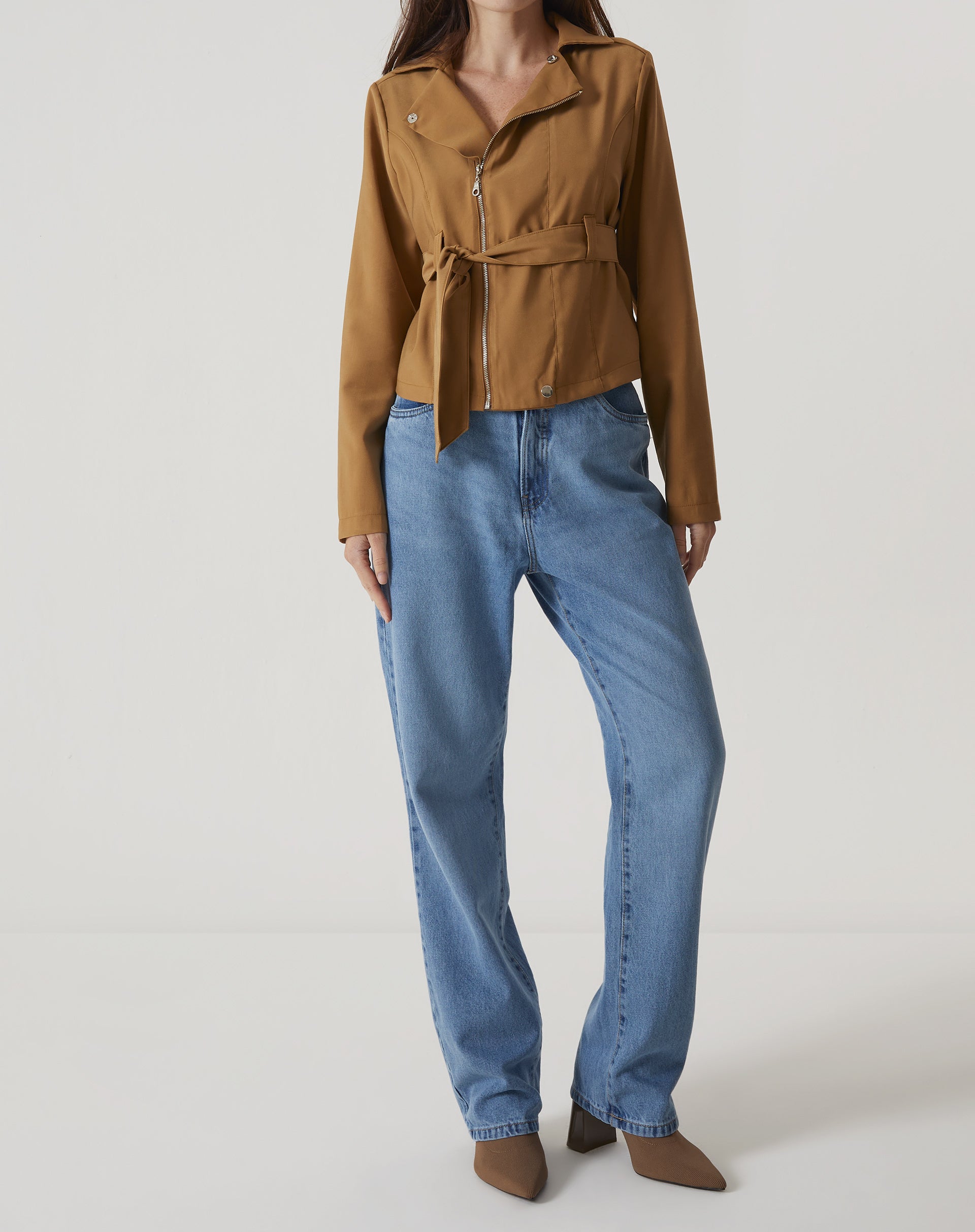 Modelo vestindo calça jeans reta azul médio com jaqueta marrom.