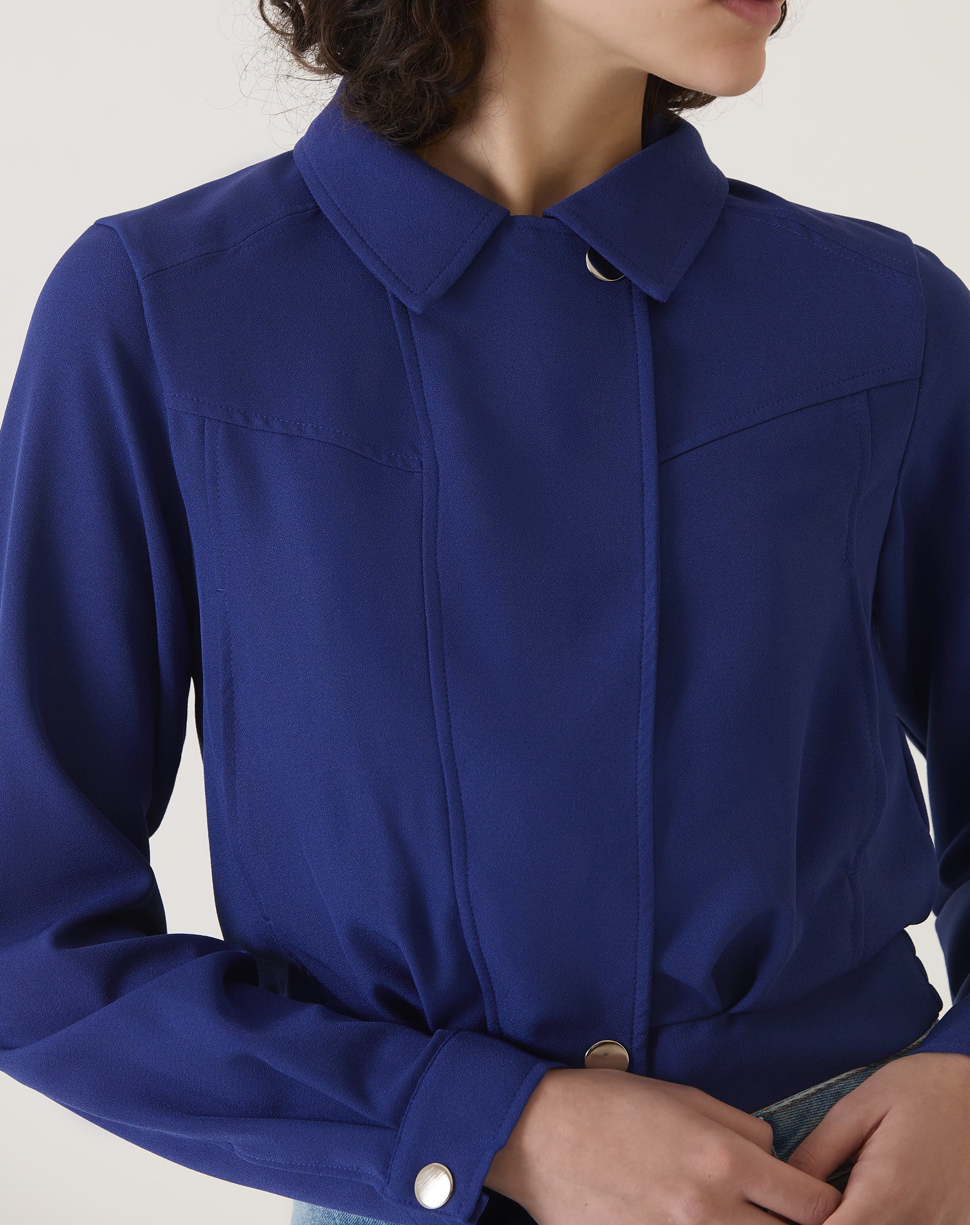 Detalhe do colarinho clássico e fechamento por botões da jaqueta azul escuro.