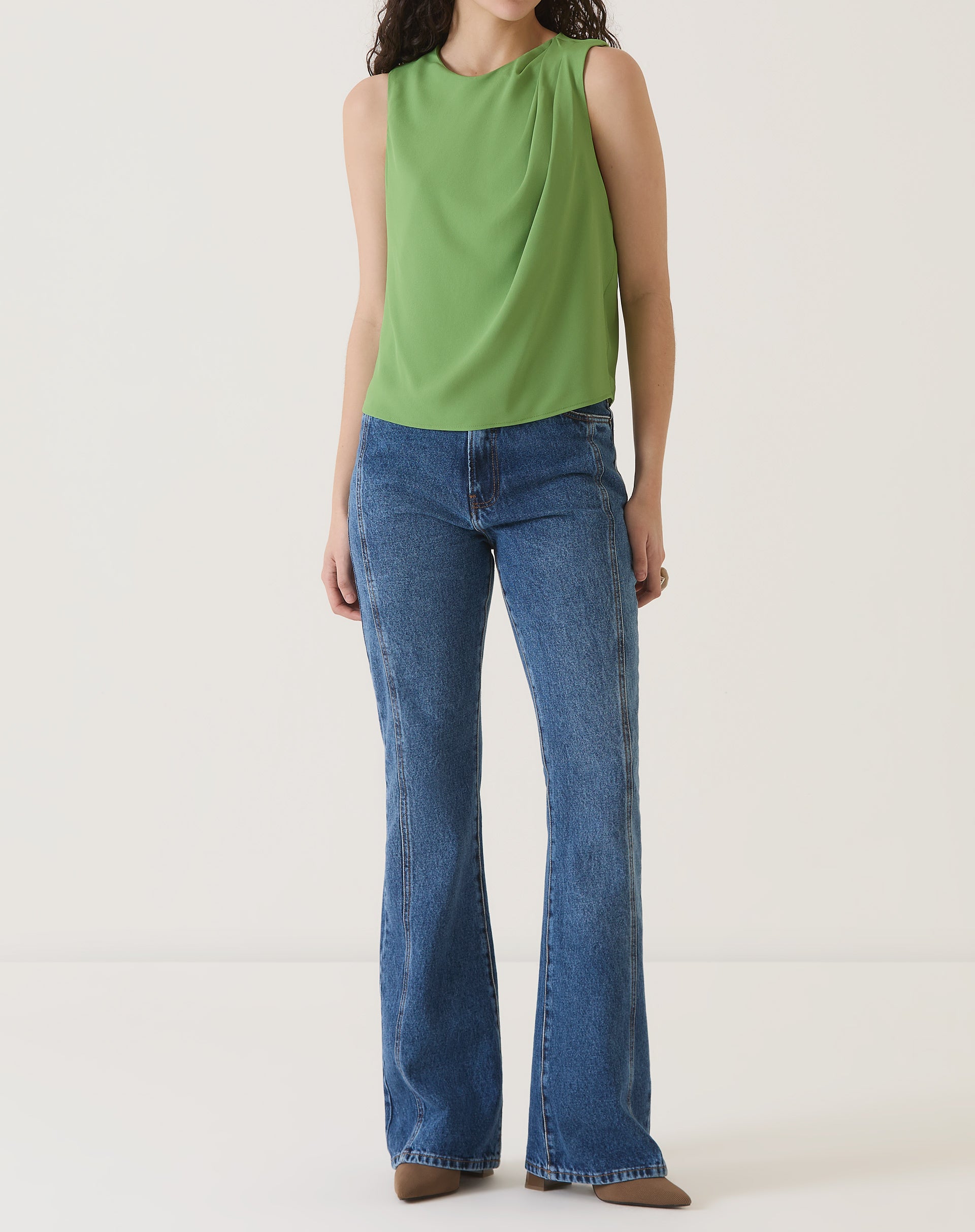 Modelo vestindo a blusa sem mangas de crepe verde com calça jeans, mostrando o look completo.