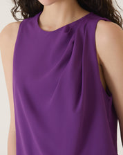 Detalhe do decote redondo e tecido fluido da blusa sem mangas de crepe roxo.