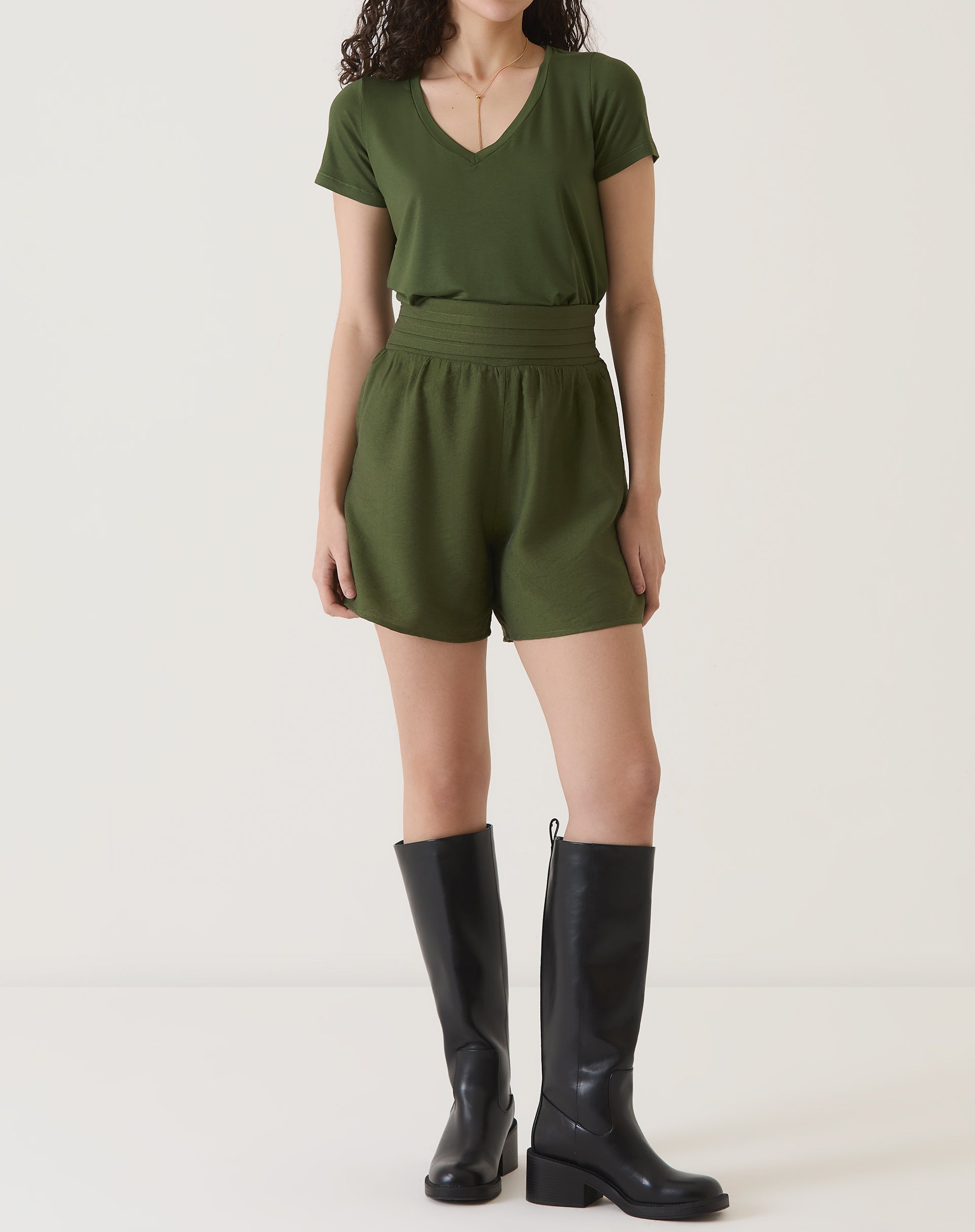 Modelo vestindo camiseta verde com decote em V e shorts combinando, vista frontal.