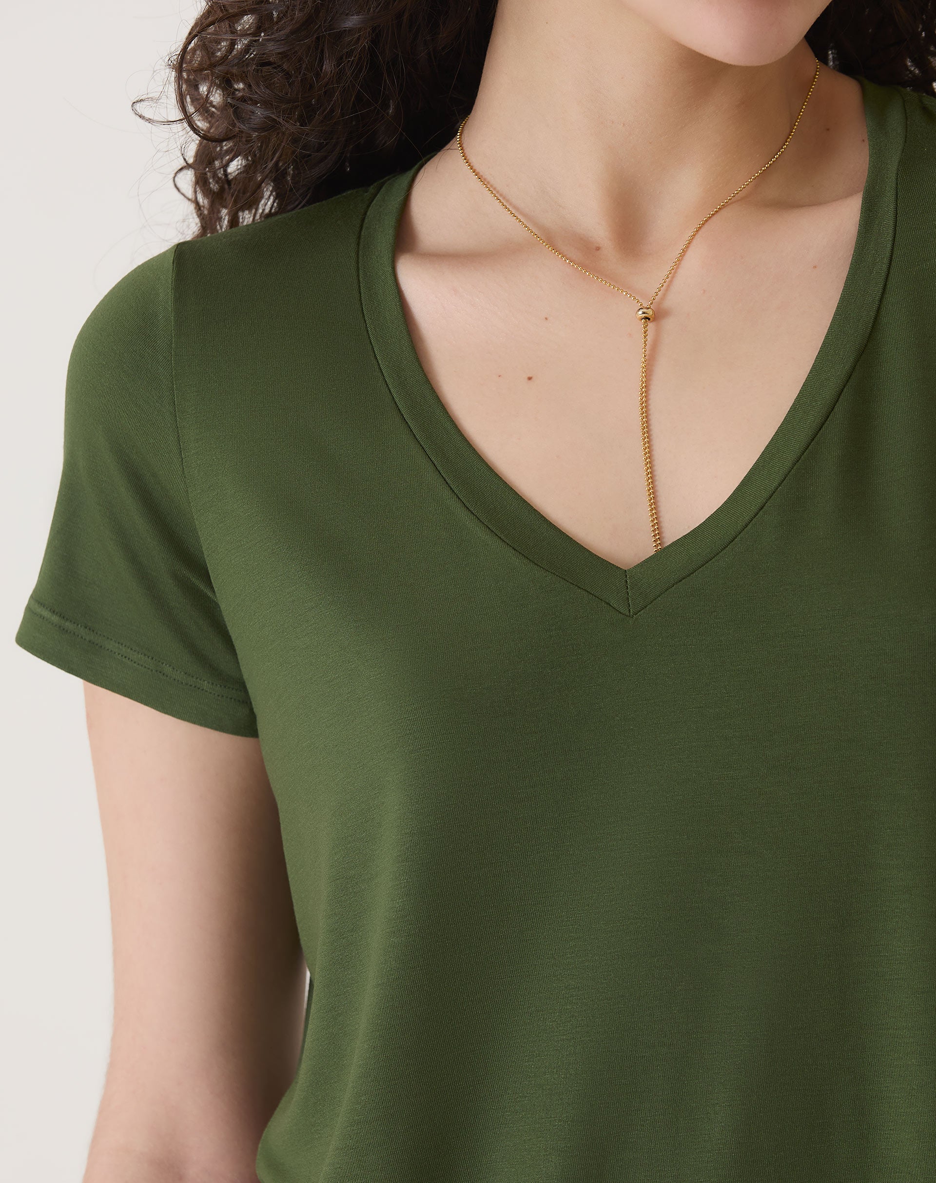 Vista lateral da camiseta verde com decote em V, destacando o caimento.