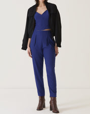 Conjunto azul com blusa de alças e calça de alfaiataria, acompanhado de jaqueta preta e botas marrons.