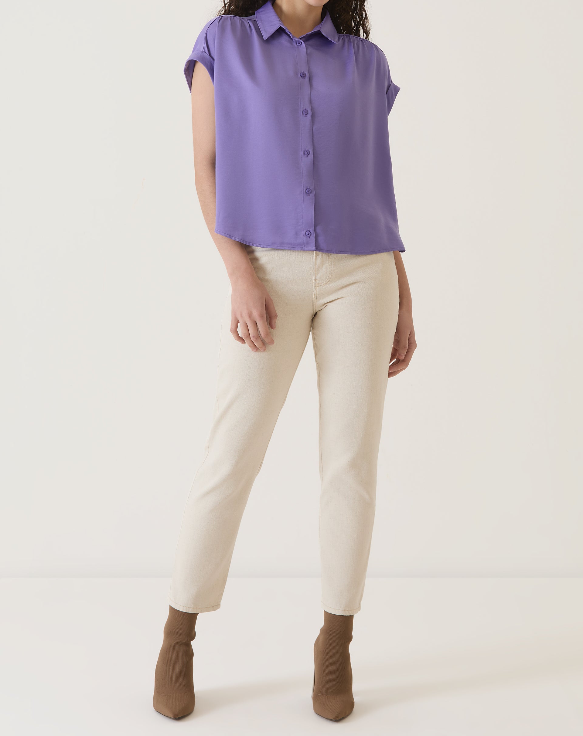 Modelo vestindo camisa de cetim roxa com calça clara e botas.