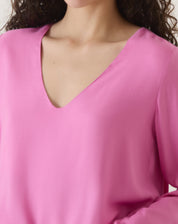 Close-up do decote V da blusa rosa, evidenciando o design minimalista.