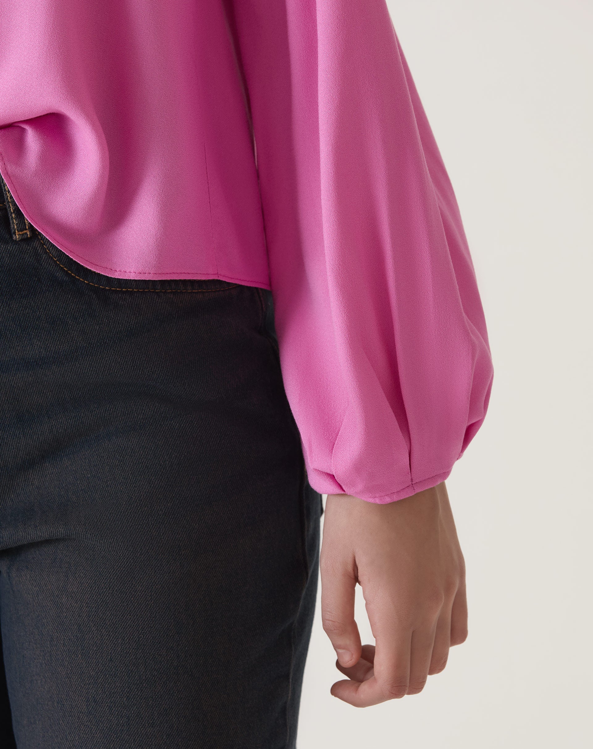 Detalhe da manga longa da blusa rosa, mostrando o tecido fluido e acabamento.