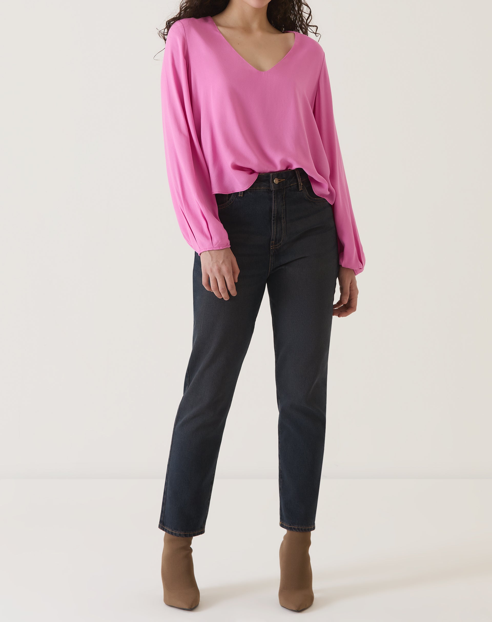 Modelo vestindo blusa rosa manga longa com decote V, combinada com calça jeans escura e botas marrons.
