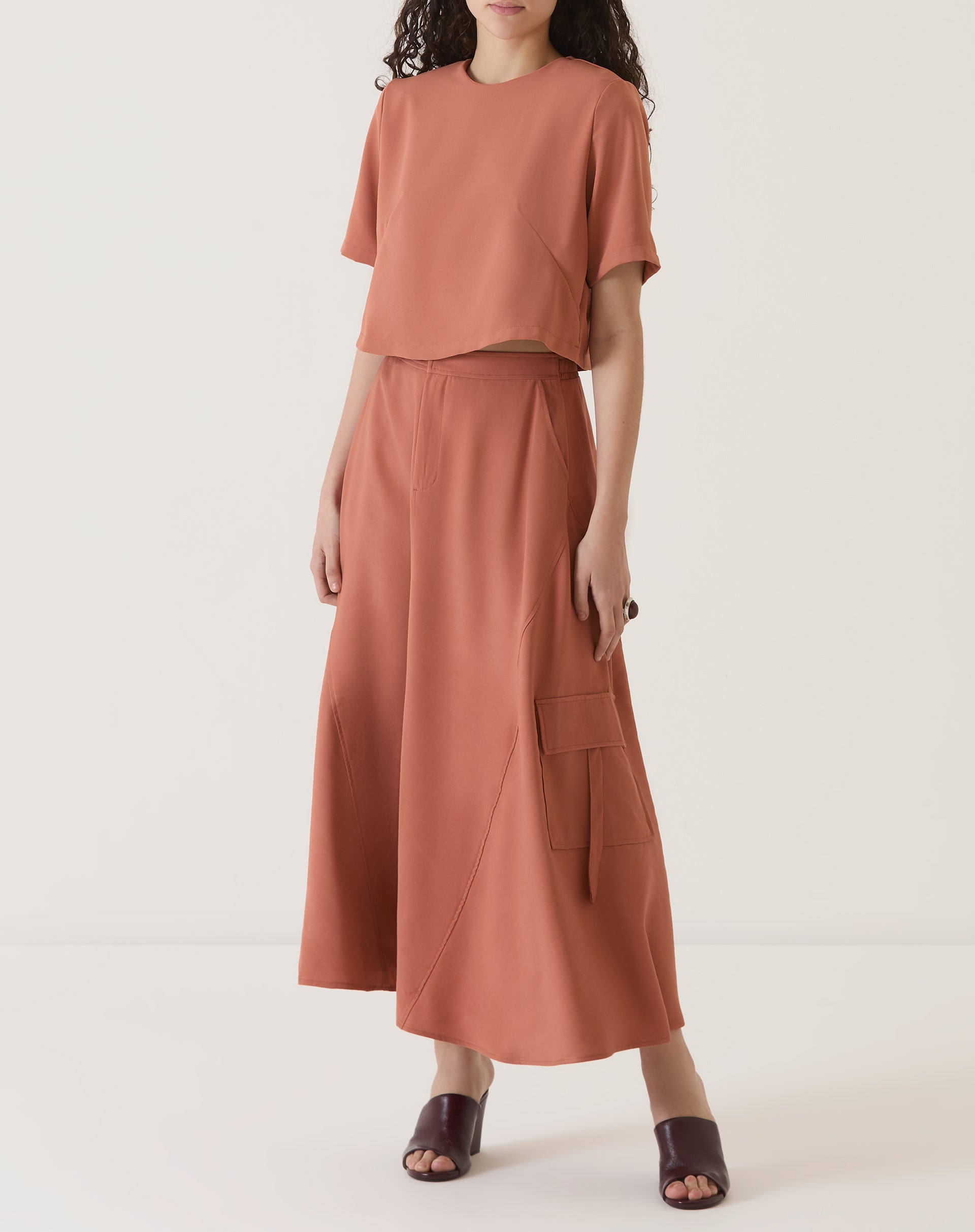 Modelo vestindo blusa cropped manga curta vinho com saia combinando.