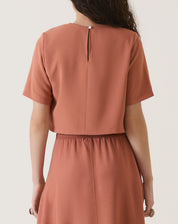 Vista traseira da blusa cropped manga curta vinho com detalhe de botão.