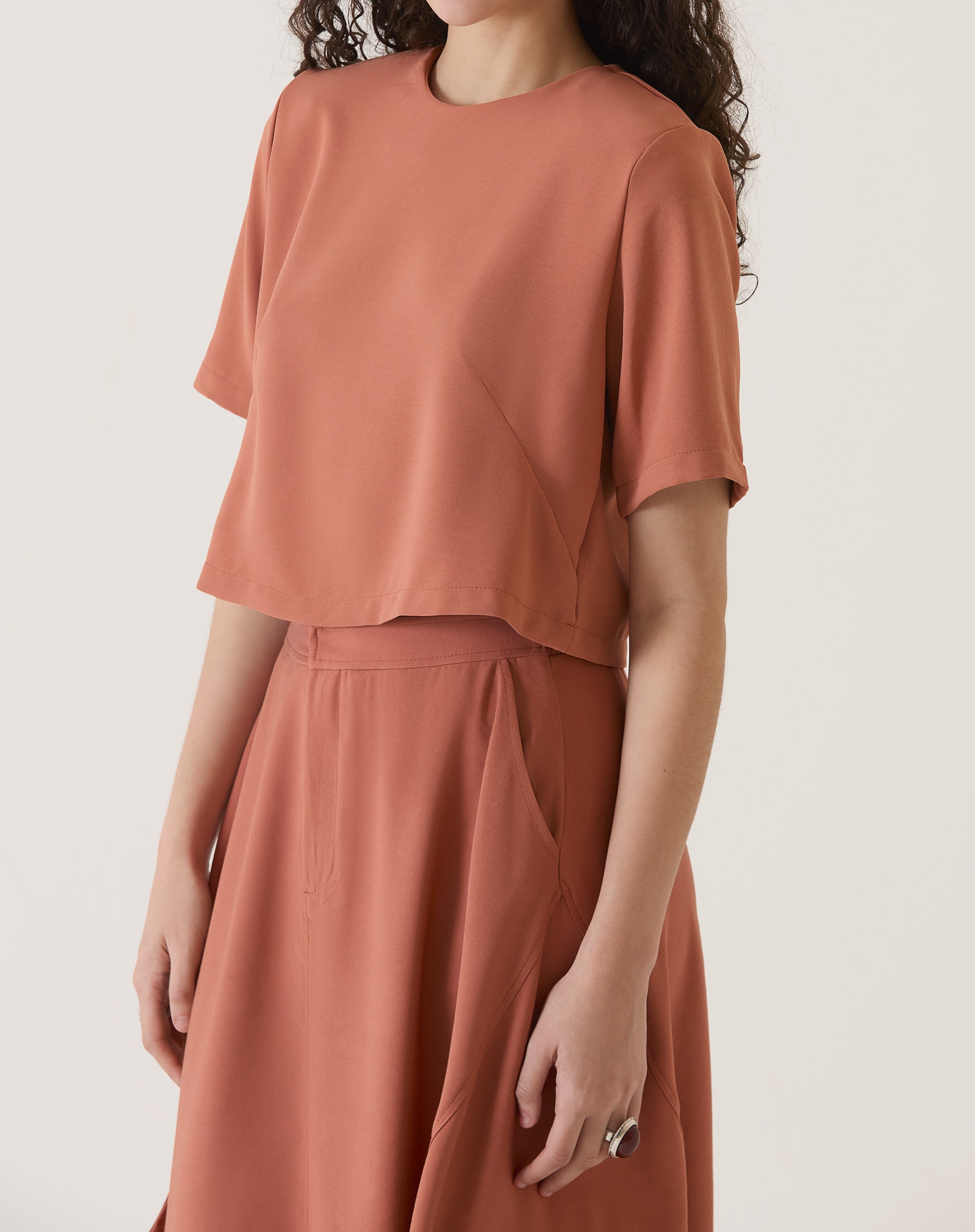 Modelo mostrando lateral da blusa cropped manga curta vinho com saia combinando.