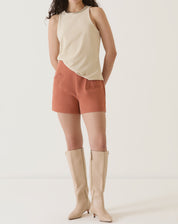 Modelo vestindo shorts de alfaiataria vinho com blusa bege e botas altas.