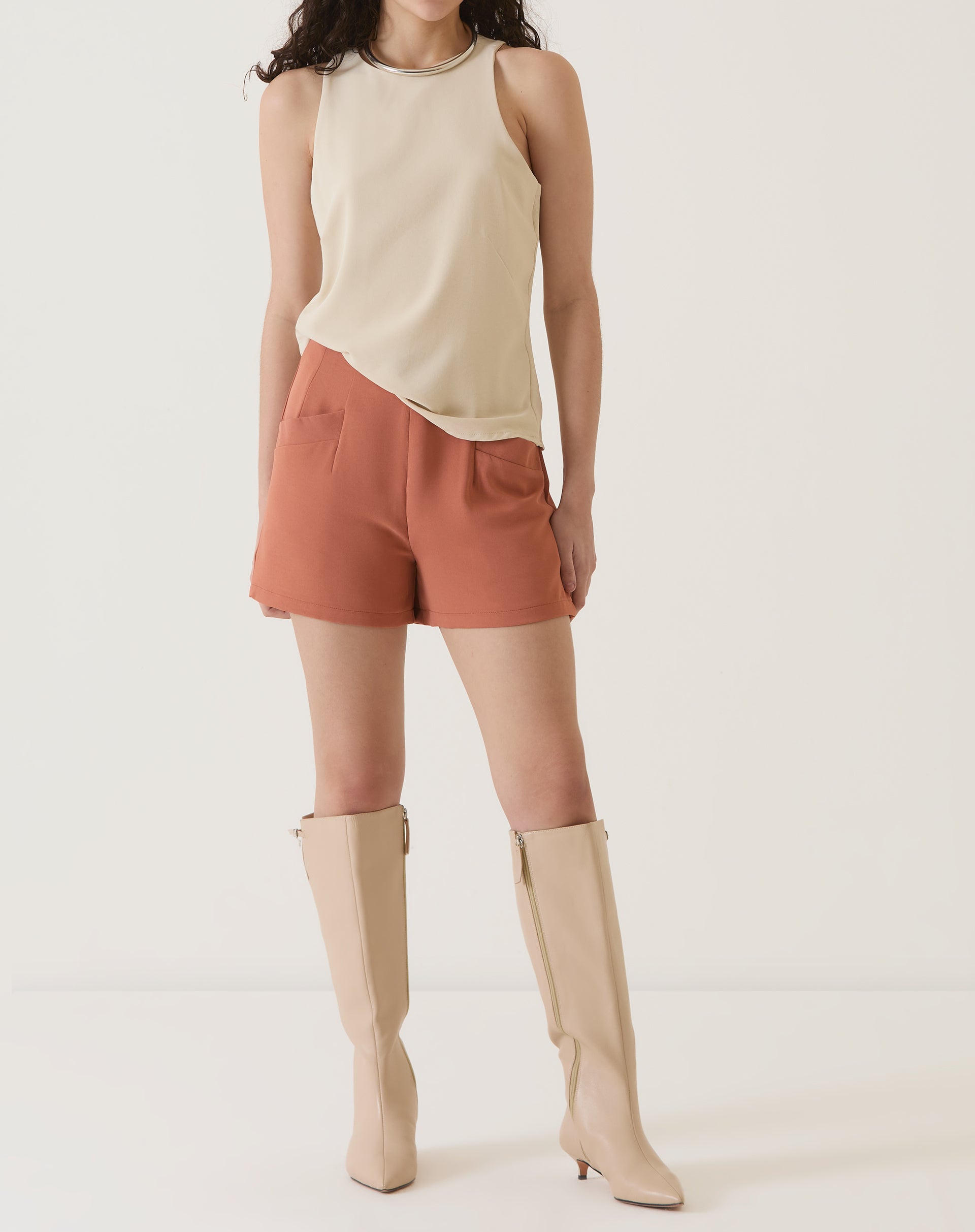 Modelo em pose casual vestindo shorts de alfaiataria vinho com botas altas.