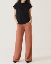 Modelo vestindo calça de alfaiataria terracota com blusa preta, vista frontal.