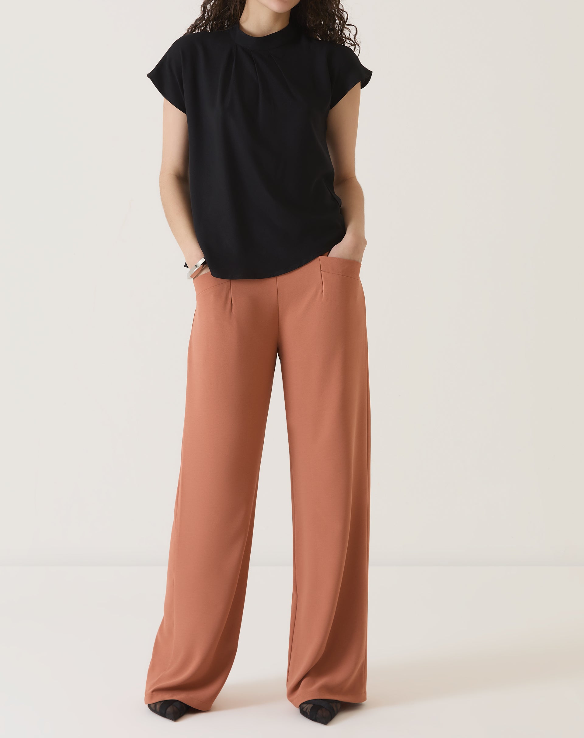 Modelo vestindo calça de alfaiataria terracota com blusa preta, vista frontal.