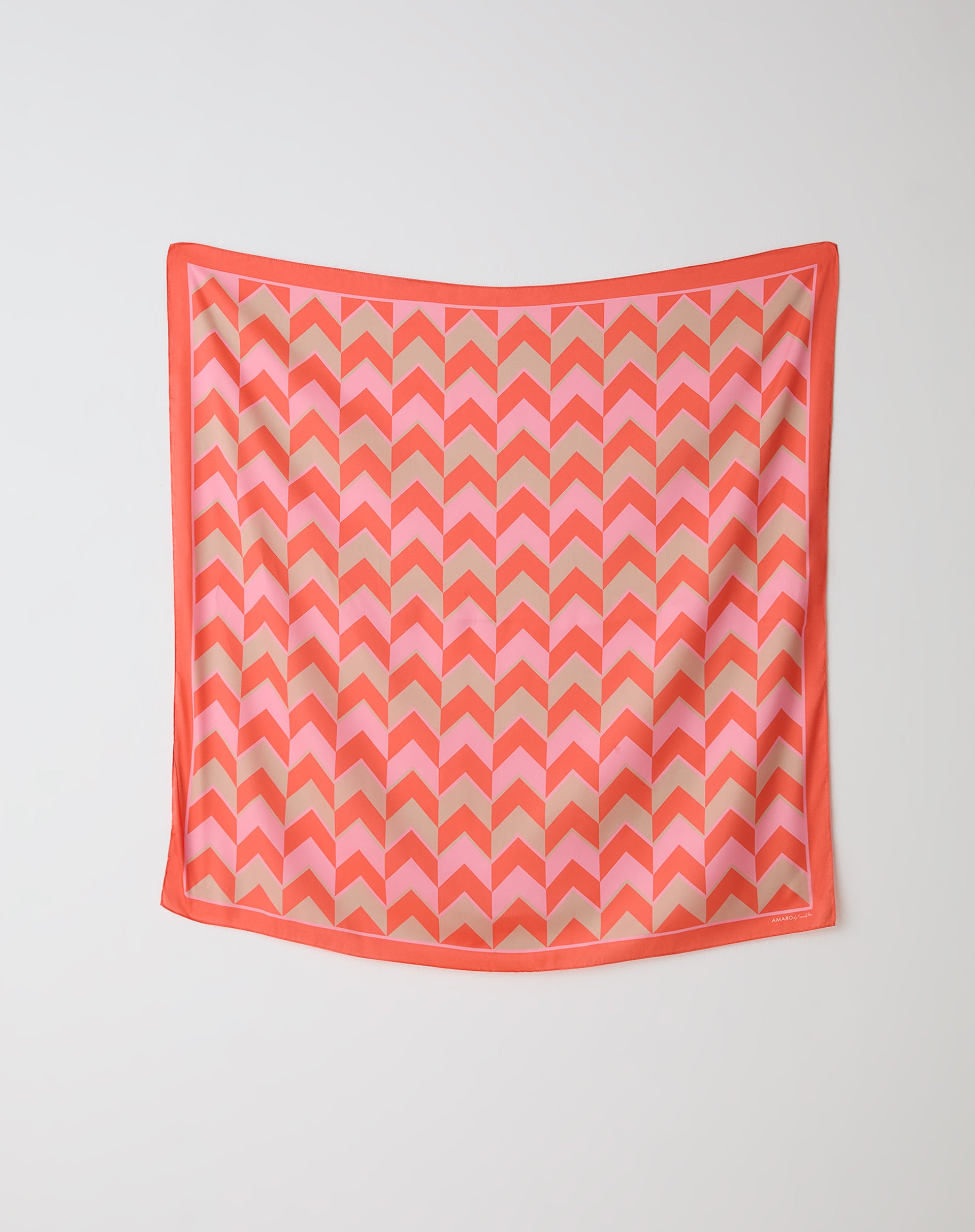 Lenço quadrado AMARO by Scarf Me 90x90cm exibido estendido na parede com estampa chevron coral, rosa e bege, mostrando padrão geométrico e borda coral.