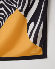 Close-up do canto do lenço mostrando barrado preto, assinatura AMARO e contraste entre a estampa zebra e o campo amarelo mostarda