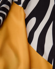 Detalhe do tecido acetinado do lenço com dobras, destacando o padrão de listras de zebra em preto e branco e a área amarelo mostarda