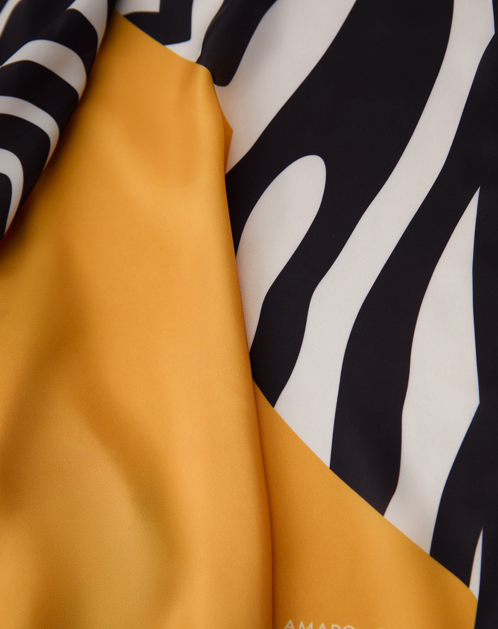 Detalhe do tecido acetinado do lenço com dobras, destacando o padrão de listras de zebra em preto e branco e a área amarelo mostarda