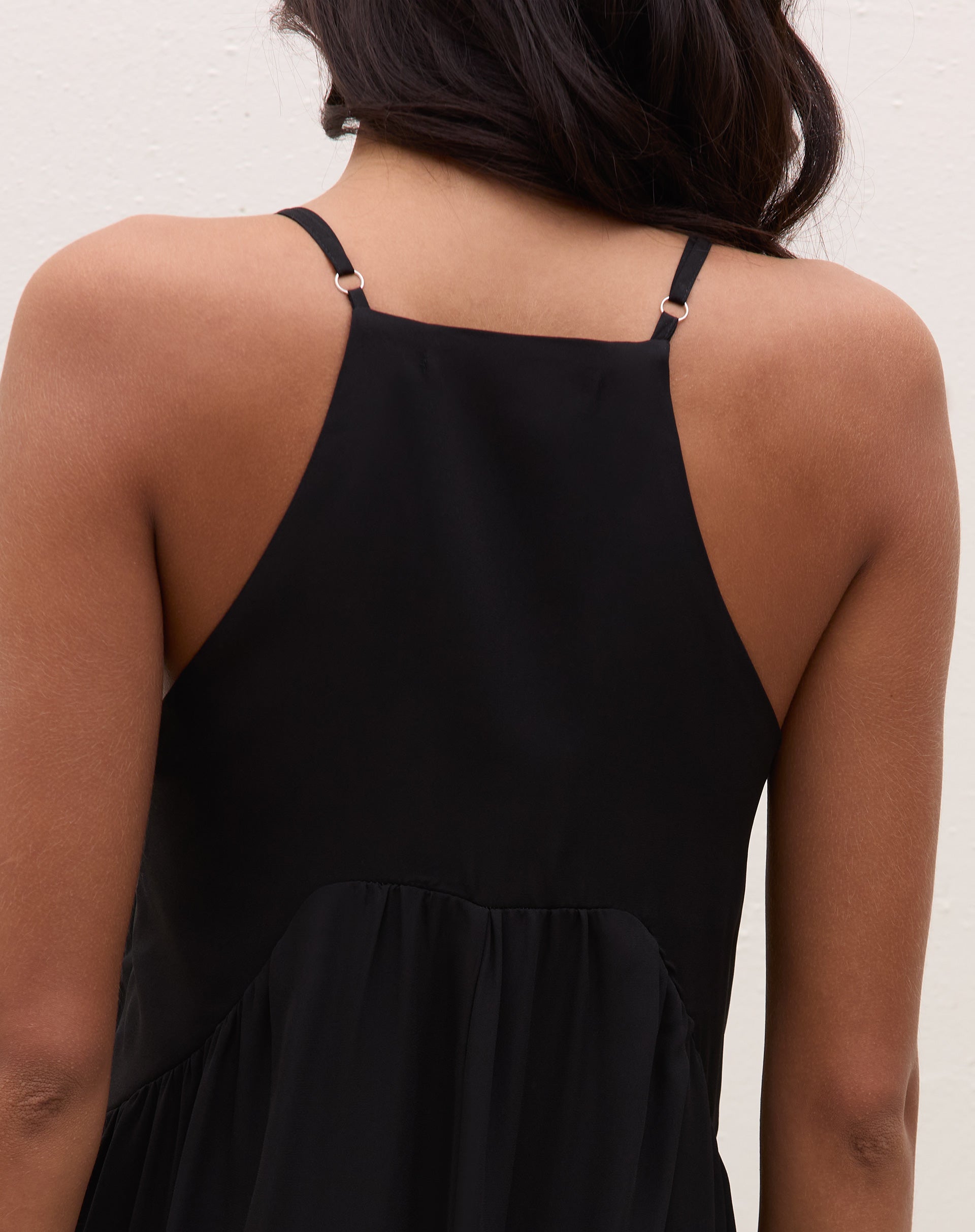 Visão traseira do vestido maxi preto mostrando costas regata, alças finas ajustáveis e saia longa com babado na barra