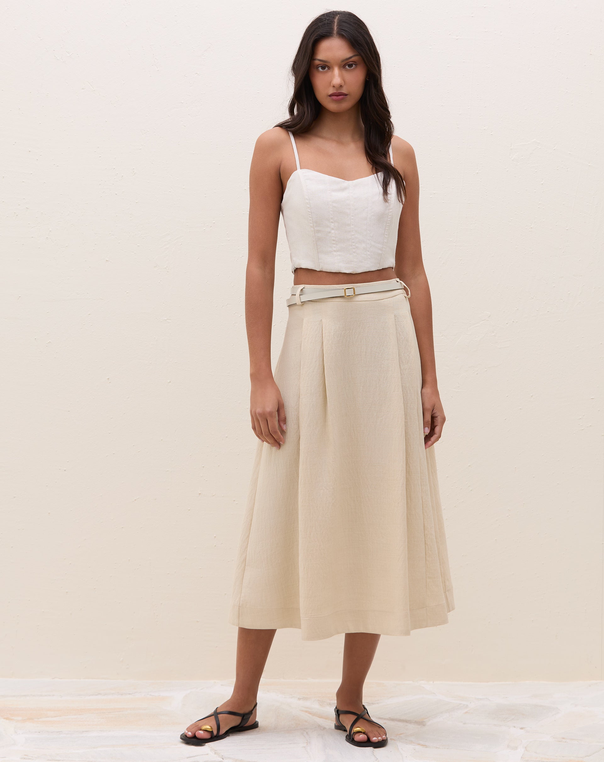 Look completo frontal com top de alcinha estruturado areia, saia midi em tom areia, cinto fino e sandália rasteira