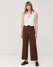 Look com colete branco cropped combinado com calça larga marrom e mocassim, estilo urbano e sofisticado