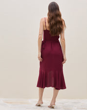 Detalhe frontal do babado assimétrico e da fenda envelopada do vestido midi transpassado vinho, evidenciando o movimento do tecido.