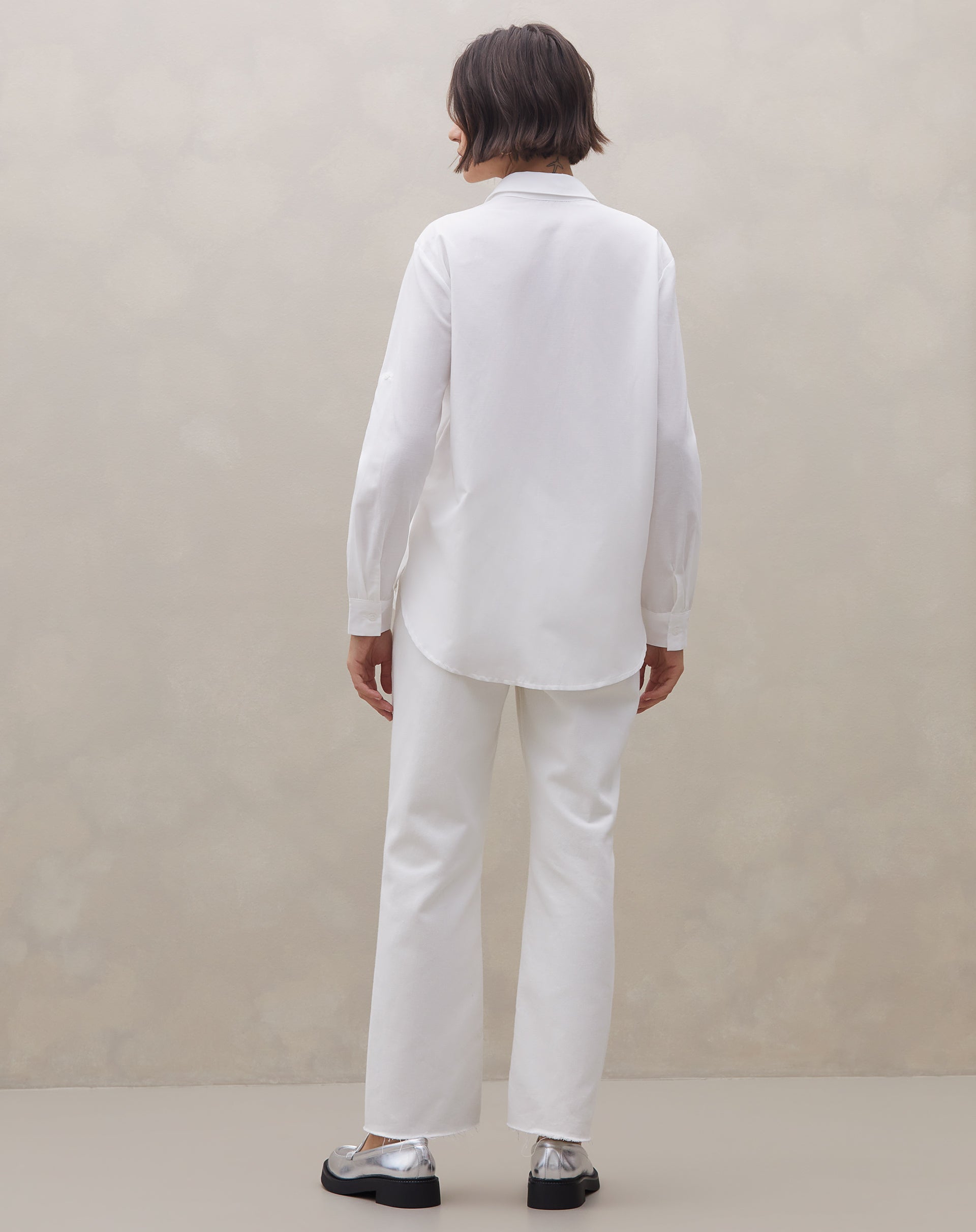 Close lateral da camisa off-white mostrando gola clássica e acabamento de manga com passador e botão - tecido fluido