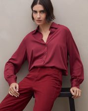 Camisa feminina manga longa em viscose vinho, modelo sentada em look monocromático com calça vinho, mostrando caimento fluido